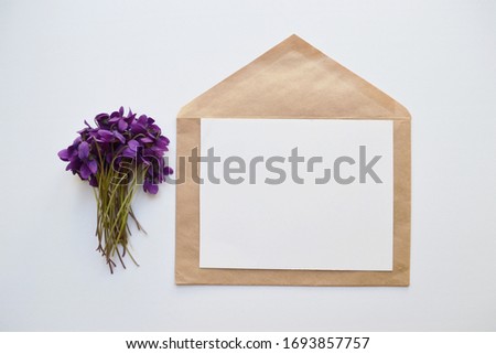 Artistic mockup for your artwork with beautiful flowers, kraft paper envelope and empty card  shot from the top. Flat lay minimalistic composition with space for text. Viola canina.