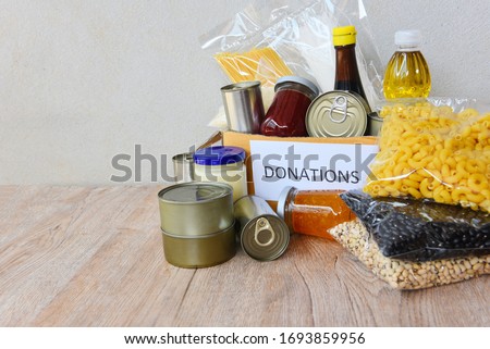 Donations box with canned food on wooden table background / pasta canned goods and dry food non perishable with pea cooking oil rice noodles spaghetti macaroni donations food concept Royalty-Free Stock Photo #1693859956