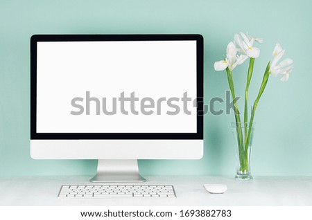 Spring home office for business with blank pc, keyboard, mouse and white fresh flowers in glass vase in light green mint menthe interior on white wood desk.