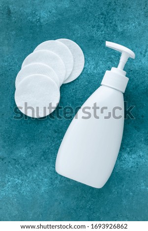 Face tonic in white plastic dispenser bottle and cotton pads on turquoise background. Makeup remover, skin care concept.