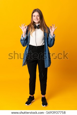 Student ukrainian teenager girl over isolated yellow background showing an ok sign with fingers