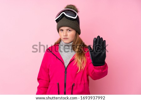 Ukrainian teenager skier girl with snowboarding glasses over isolated pink background making stop gesture with her hand