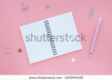 open notebook in a box on a spring on a pink background and stationery around. Space for text. Flat layout.
