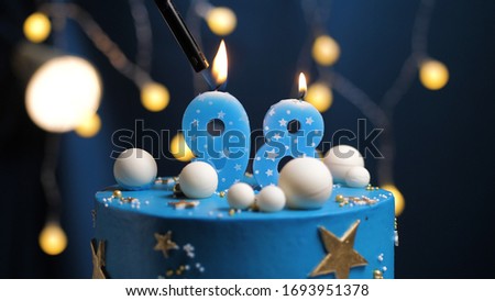 Birthday cake number 98 stars sky and moon concept, blue candle is fire by lighter. Copyspace on right side of screen. Close-up view