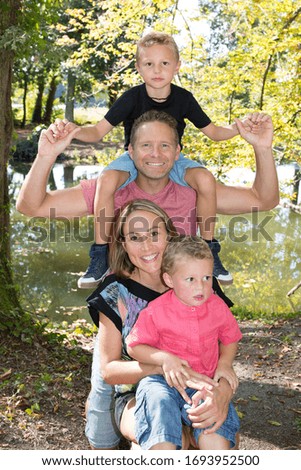 family four in park parents giving piggyback ride pose with children