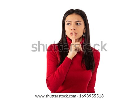 Closeup photo of beautiful young woman, holding index finger near her lips, asking to keep silence, looking to the side, isolated on white background