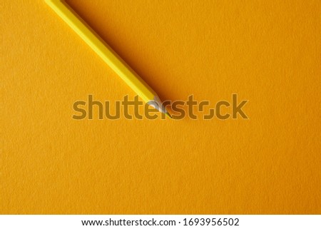Yellow colored pencil lying on a bright yellow background, macro photography.