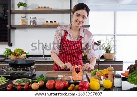 Pictures of beautiful woman standing in the kitchen cooking The menu she will cook is salmon steak and vegetable salad. Modern woman kitchen concept