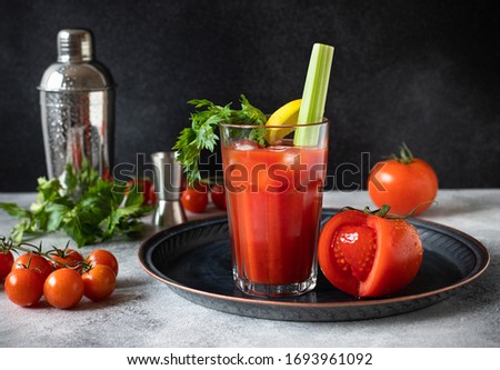 Classic alcoholic cocktail Bloody Mary with ice, lemon and celery. Cocktail ingredients and bar tools on a gray table and black background