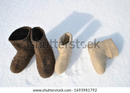 A pair of felt boots is standing in the snow. Valenok lies in the snow. Boots top view. White and brown shoes. Valenoks are covered with small ice floes. Snow stuck to the boots.