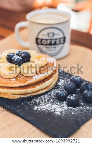 Delicious pancakes with blueberry, bananas and maple syrup on black dish