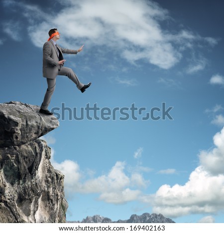 Businessman in a blindfold stepping off a cliff ledge concept for risk, challenge, conquering adversity or ignorance Royalty-Free Stock Photo #169402163