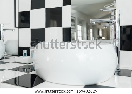 Modern white oval sink in a bathroom with checkered black and white tiles.
