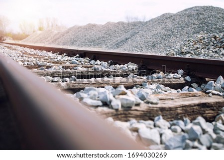 Railroad construction site. Railway tracks with wooden rail ties and ballast. In background large pile of ballast rocks used for building railroads. Royalty-Free Stock Photo #1694030269