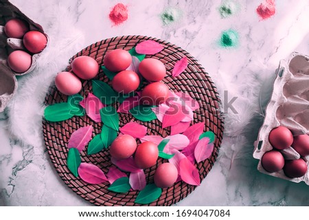 Colorful Easter composition of the chicken eggs, colored birds feathers, dyes for eggs on the marble table. Preparing for the easter holiday. Top view, flat lay image with festive atmosphere.