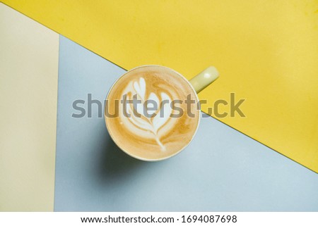 Freshly prepared latte with layers of milk, coffee and foam in a yellow glass on a colored background. Coffee picture for menu