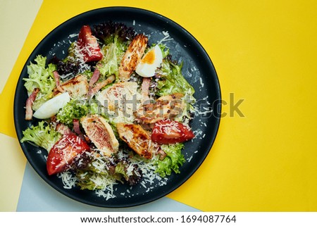 Caesar salad with croutons, parmesan, chicken, egg in black plate on colored background. Restaurant serving. Close up
