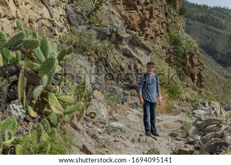 A young man with a backpack travels along a route in the west side of Tenerife. Hiking by the mountain trail surrounded by endemic vegetation and fields of lava rocks. Canary Islands, Spain.