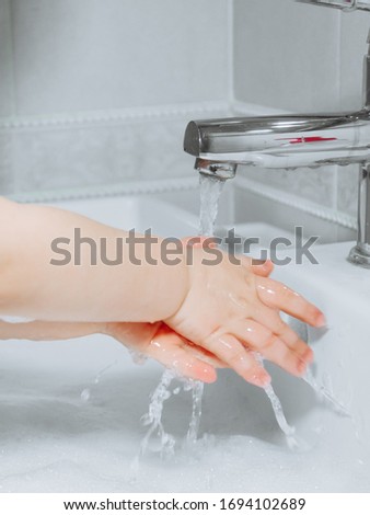 Little girl washes her hands in a white sink with water and soap. Water flows into the hands. Coronavirus Prevention.