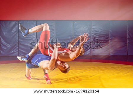 Two strong wrestlers in blue and red wrestling tights are wrestlng  on a wrestling carpet in the gym. Young man doing grapple.