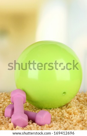 Bright ball and dumbbells on carpet on bright background