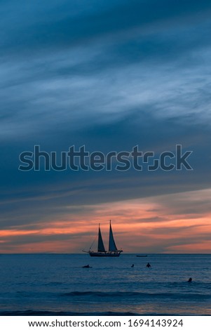 Sunset in Tamarindo with bathers, surfers and a sailboat in the background. Pura Vida scenes in Costa Rica. Central America.
