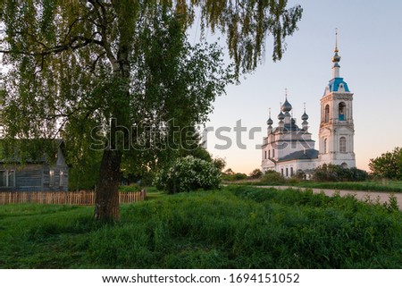 Russian rural landscape with an old church, a birch and a wooden house in spring morning