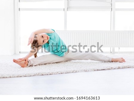 Beautiful little girl performing acrobatics in bright room