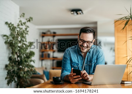 Portrait of a cheerful man using smart phone at home office. Royalty-Free Stock Photo #1694178241