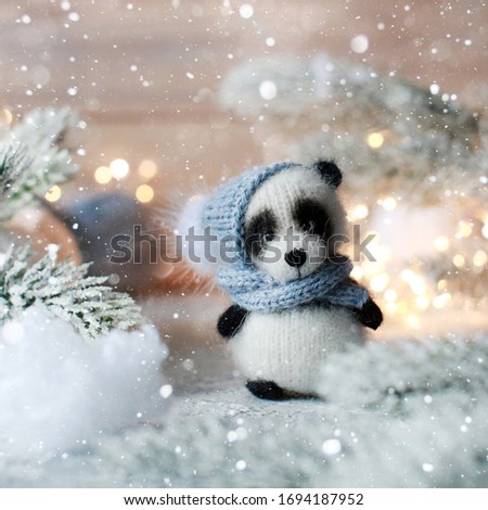 Handmade knitted panda bear. Panda bear in a scarf and hat with a pumpon among the decorative Christmas trees. Winter composition