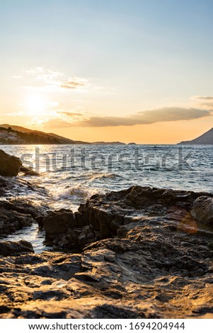 Waves at Sunset in Croatia, sun setting on the water surface of the sea on the rocky shore, the sun among the stones in the water