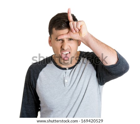 Closeup portrait of funny man displaying a loser sign on his forehead and looking at you with disgust at camera gesture, isolated on a white background. Negative emotion facial expression feelings