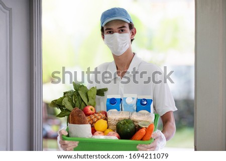 Food delivery during corona virus outbreak. Courier wearing face mask delivering grocery order in coronavirus epidemic. Safe shopping in pandemic. Takeout meal. People stockpile food. Royalty-Free Stock Photo #1694211079