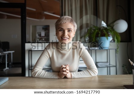 Portrait of happy attractive young businesswoman with short haircut sitting at table, looking at camera. Web cam view skilled female worker holding video call meeting with partners or client from
