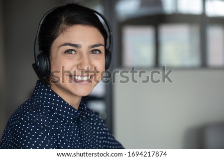 Head shot close up smiling attractive indian ethnicity millennial businesswoman wearing headphones, looking at camera. Happy sincere pleasant young mixed race female professional working remotely. Royalty-Free Stock Photo #1694217874