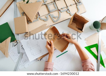 Top view of woman hand with box on the designer's desk, she designs new packaging Royalty-Free Stock Photo #1694230012