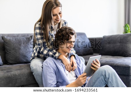 Beautiful couple is using a l tablet and smiling while sitting on the couch at home