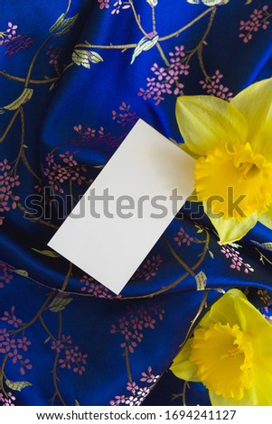 Mock up - Background luxury blue  silk with white card and yellow flowers. Satin velvet material or luxurious background or elegant wallpaper. Trend classic blue color of the year 2020