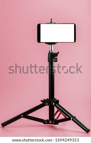 Mobile phone mounted on a tripod with a white display free for images and text, pink isolated background.