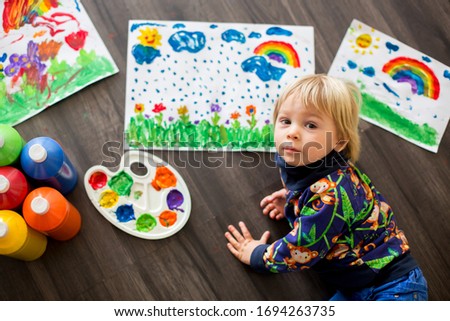 Sweet toddler blond child, boy, painting with colors, making finger prints on the paper