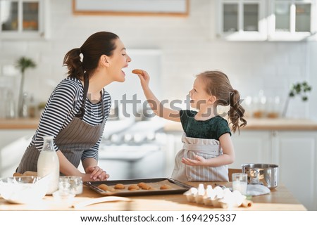 Happy loving family are preparing bakery together. Mother and child daughter girl are cooking cookies and having fun in the kitchen. Homemade food and little helper.                                 Royalty-Free Stock Photo #1694295337