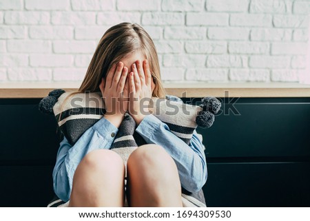 Sad Caucasian girl in depression hugs a pillow and closes her eyes with her hands on a background of a white brick wall. Thinks about the problems and puberty of a teenage girl. Adolescence period Royalty-Free Stock Photo #1694309530