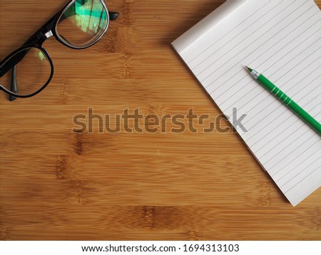 Top view wood desk with eyeglasses paper and pen. Blank space for insert copy text.