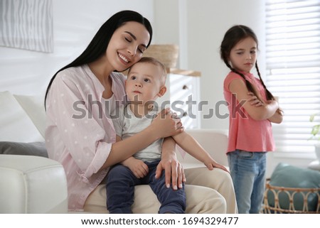 Unhappy little girl feeling jealous while mother spending time with her baby brother at home