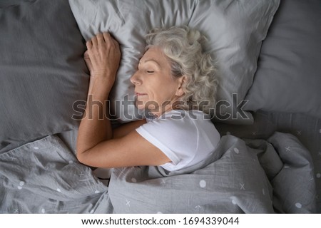 Above top view calm peaceful elderly mature hoary woman sleeping on soft pillow under blanket, enjoying sweet dreams at night. Happy middle aged granny lying on side, resting in comfortable bed alone. Royalty-Free Stock Photo #1694339044