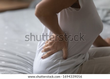 Close up unhealthy elderly woman touching lower back, feeling backpain after waking up in morning, sleeping on uncomfortable mattress. Mature senior grandmother suffering from arthritis radiculitis. Royalty-Free Stock Photo #1694339056