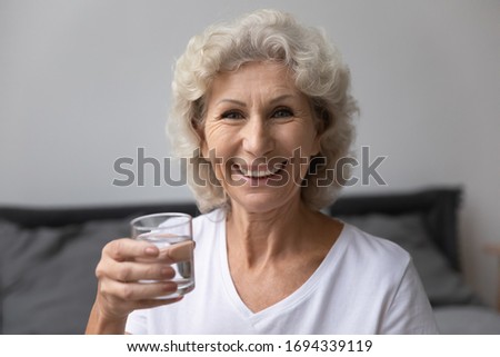 Head shot close up portrait happy senior elderly woman holding glass of fresh pure distilled water, looking at camera. Smiling middle aged grandmother enjoying healthy habit, drinking aqua every day. Royalty-Free Stock Photo #1694339119