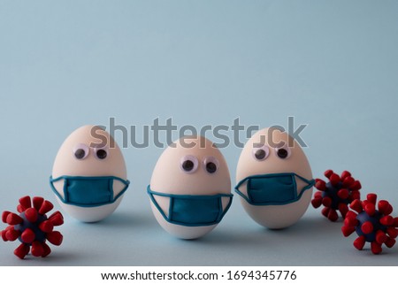 Eggs wearing medical mask for stop coronavirus and models of covid-19 virus on blue background. Epidemic coronavirus COVID-19 concept. Place fo text Royalty-Free Stock Photo #1694345776