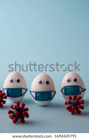 Eggs wearing medical mask for stop coronavirus and models of covid-19 virus on blue background. Epidemic coronavirus COVID-19 concept. Place fo text Royalty-Free Stock Photo #1694345791