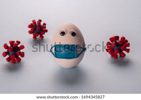 Eggs wearing medical mask for stop coronavirus and models of covid-19 virus on blue background. Epidemic coronavirus COVID-19 concept. Place fo text Royalty-Free Stock Photo #1694345827